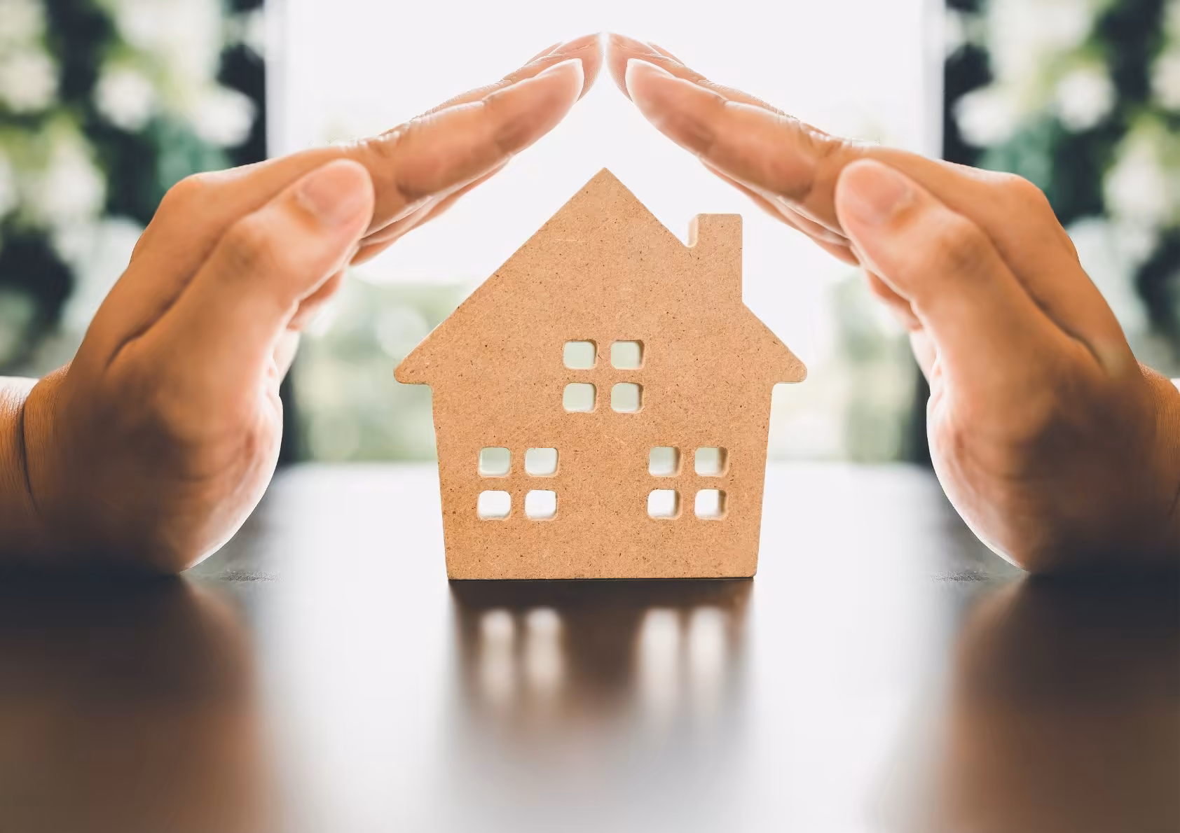 a cutout of a home with hands protecting it. First time homebuyers or foreclosure home buying. 