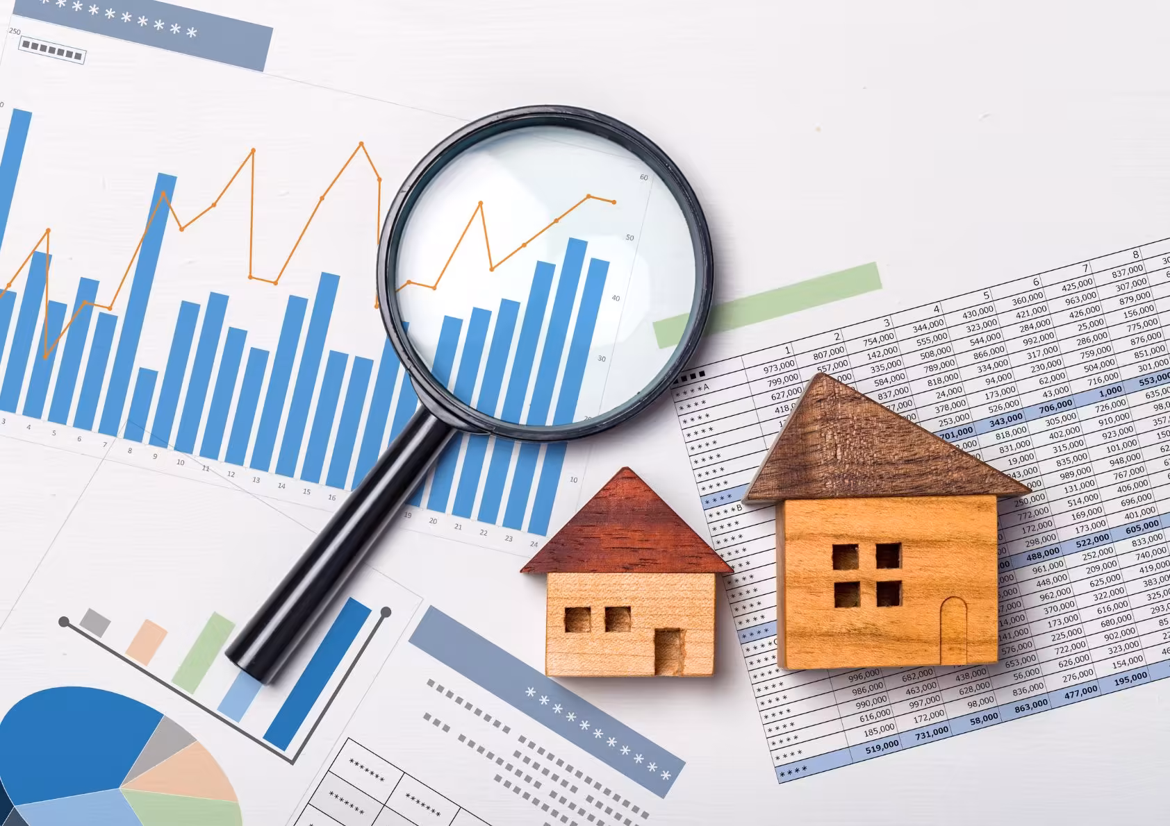graphs with magnifying glass with toy houses depicting the housing market.