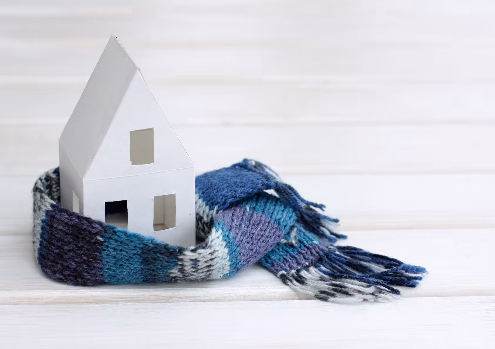 Tiny model home wrapped in a scarf. Depicting a home in winter